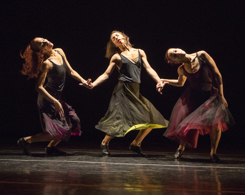 Women in long skirts sway together by holding one another's hands